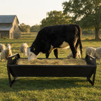 Mincy Pets 22-gallon black galvanized steel livestock hay feeder with a V-shaped trough in a sunny farm pasture.
